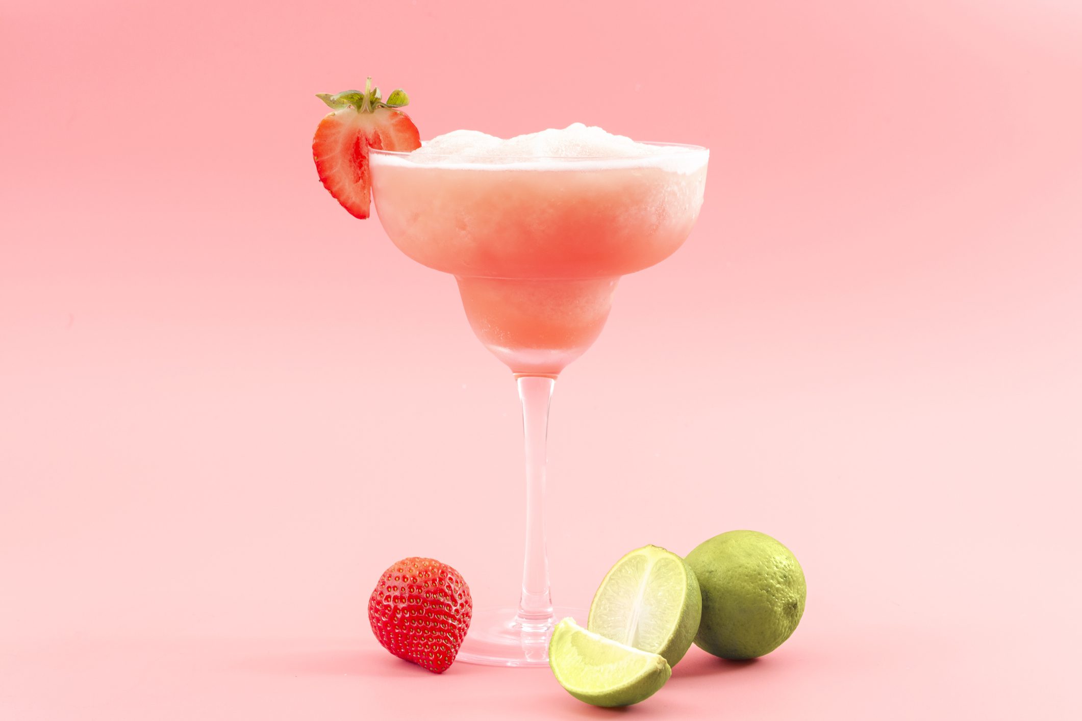 Mixed cocktails, party punch smoothies and frozen summer drinks concept with strawberry mojito or daiquiri in margarita glasses, strawberries and limes isolated on pink background